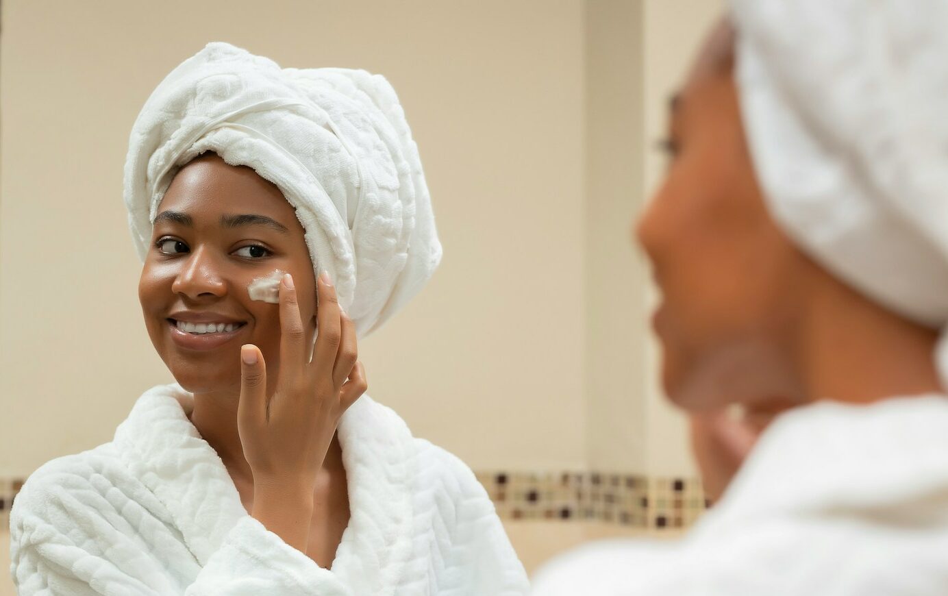 Photo by Kaeme a woman with a towel on her head and a jar of cream on her face